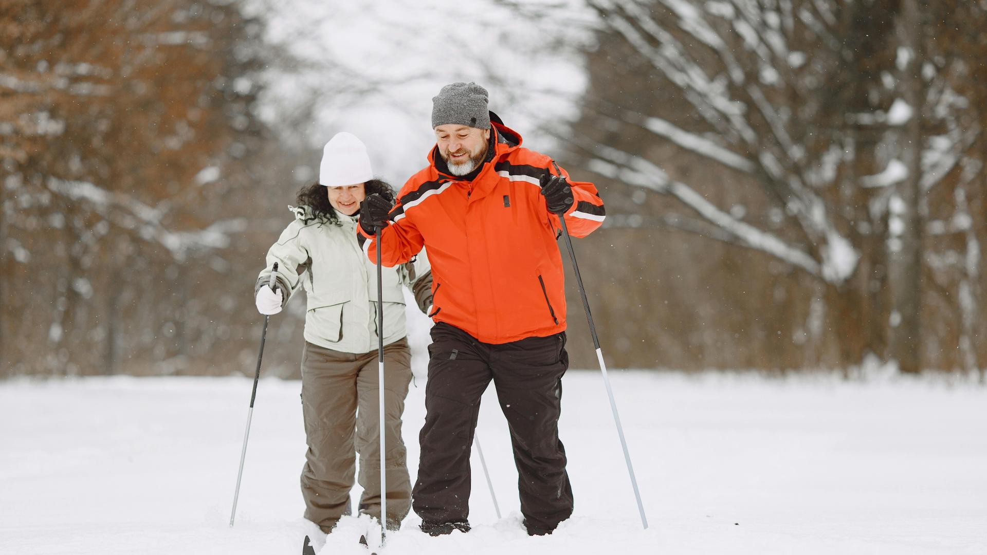 Two people skiing in a snowy forest, smiling and wearing winter gear.